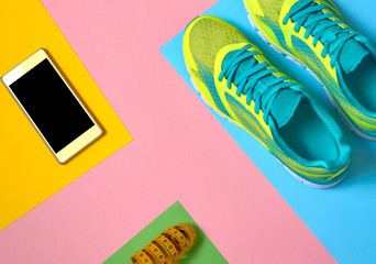 Fototapeta na wymiar Close up of running shoes, mobile smart phone with black screen and measuring tape on colorful background. Top view, flat lay. Sport, fitness concept, healthy lifestyle