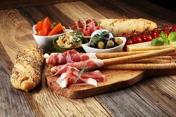 Poster Italian antipasti wine snacks set. Cheese variety, Mediterranean olives, crudo, Prosciutto di Parma, salami and wine in glasses over wooden grunge background. © beats_