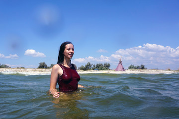 Young brunette girl in red swimsuit smiling and staring into the distance during swimming in a sea,...