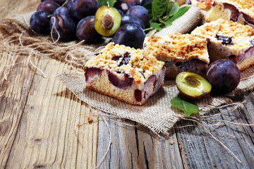 Rustic plum cake on wooden background with plums around.