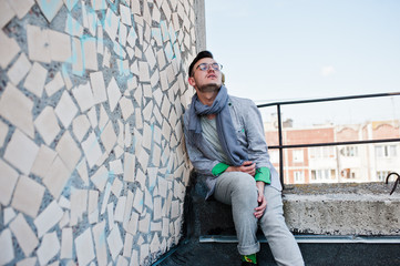 Dreamer stylish macho man in gray suit, scarf and glasses posed on the roof.