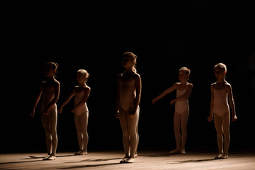 Obraz premium A group of small ballet dancers rehearses on stage with light and smoke