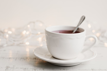 Cup of red hibiscus tea in a white mug, yellow lights on background. Herbal drink on wooden table. Tea break