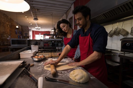 Male baker rolling a flour dough while making pasta 