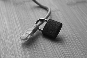 A cyber security concept image consisting of an Ethernet cable, padlock and a wooden background.  