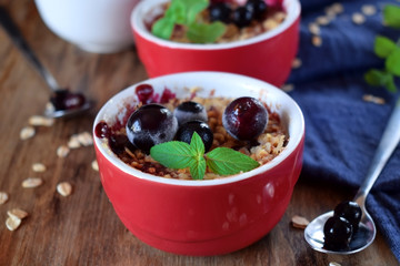 Crumble with berries in portion ceramic bowls topped with black currant and mint