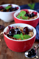 Crumble with berries in portion ceramic bowls topped with black currant and mint