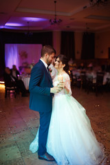 Naklejka premium Happy bride and groom and their first dance, wedding in the elegant restaurant with nice light and people on the background