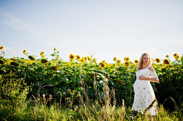 Blonde pregnant mother in sunflowers field. Happy moments of pregnancy.