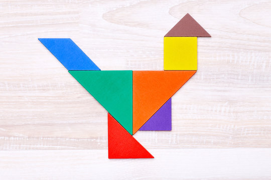 Flay lay of colorful tangram figures arranged in shape of chicken on wooden table
