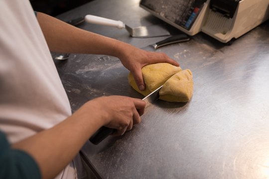 Male baker cutting dough in bakery