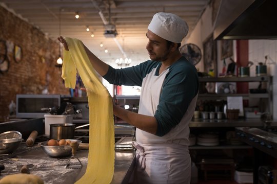 Chef holding pasta sheet while standing in kitchen