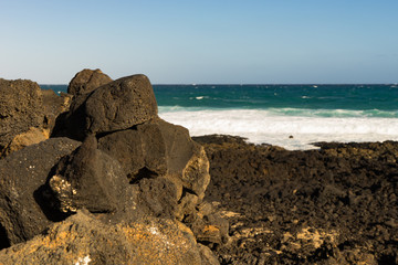 Black volcanic rocks stacked on Lanzarote beach with waves background