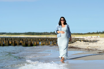 entspannte Schwangere l&auml;uft am Strand