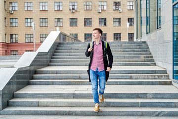 Full length body portrait of handsome male student with backpack walking down stairs and having rest in university campus  outdoors, copy space. Education, rest and relax, travel and tourism concept