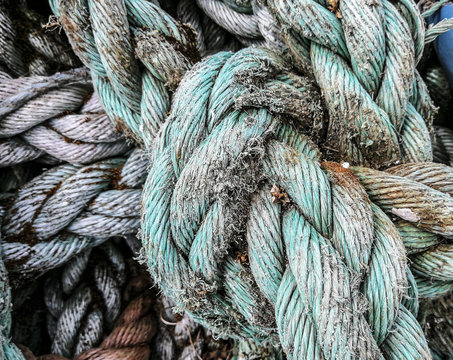 Close up image of old boating ropes, frayed and knotted in grey, turquoise with seaweed and rust stains