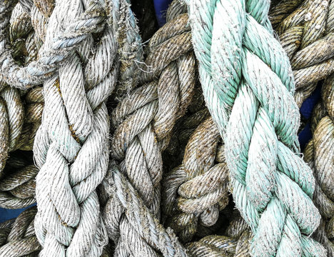 Close up image of old boating ropes, frayed and knotted in grey, turquoise with seaweed and rust stains