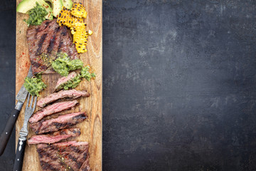 Barbecue dry aged wagyu flank steak with corn, avocado and chimichurri sauce as top view on a...