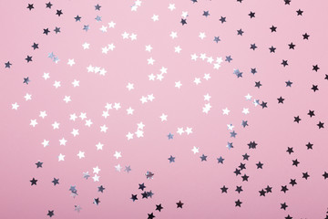 Pink background with silver star confetti. Top view.