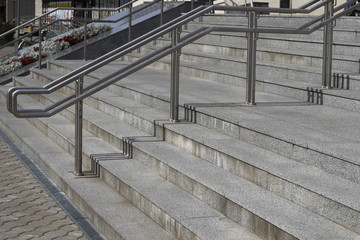 Stainless steel round, comfortable railing, marble gray steps. A flight of stairs, the entrance to a large building.