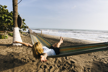 A blonde tourist enjoys the sun and sea in a hammock on the Caribbean coast of Colombia - obrazy, fototapety, plakaty