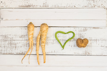 Love concept. Two human shaped parsley roots, green string-beans and potato hearts laying on the old shabby planks painted white. Background. Texture. Vegetables.