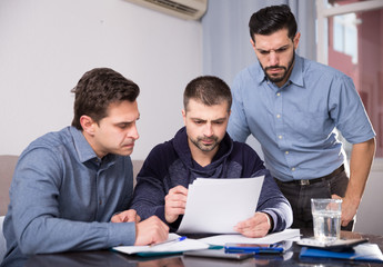 Three upset males with papers at table