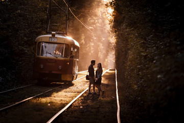 Naklejka premium Young couple, standing on the tram rails, in high trees alley in stunning evening sunlight.