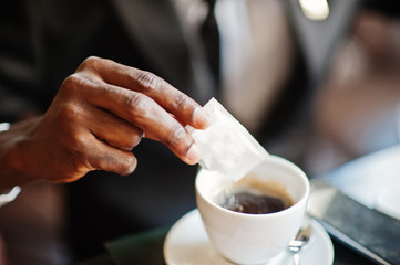 Fototapeta na wymiar Close up hand of african american business man pours sugar into coffee.