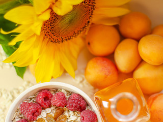 Healthy breakfast. White plate of oatmeal with dried apricots and raspberries, a glass of an apricot juice and fresh apricots on a white table.