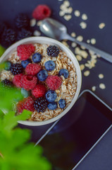 Healthy breakfast. White plate with oatmeal strewn and different berries on a blue background. Summer harvest.