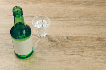 a soju bottle with glass of soju on the wooden table. Soju is the colorless distilled beverage, the...