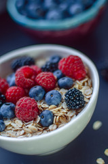 Healthy breakfast. White plate with oatmeal strewn and different berries on a blue background. Summer harvest.