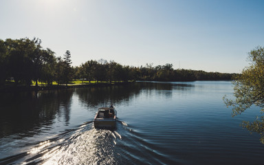 Obraz premium boat from behind driving on a beautiful river in a park during sunny summer day on toronto island