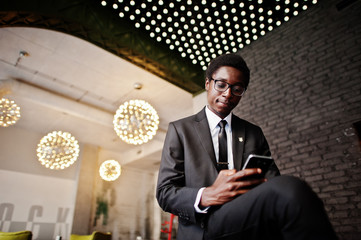 Business african american man wear on black suit and glasses at office looking on mobile phone...
