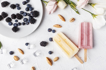Fototapeta na wymiar Homemade frozen ice cream popsicles from fruits and berries on table whith flowers and ingridients, top view