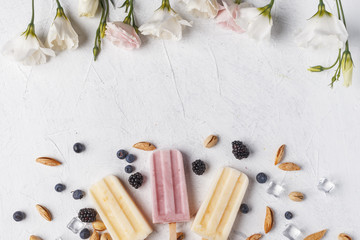 Homemade frozen ice cream popsicles from fruits and berries on table whith flowers and ingridients, top view