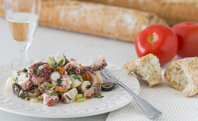 Octopus salad. Background: bread, tomatoes and a glass of white wine.