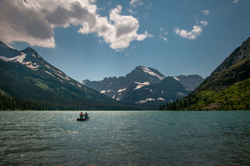 Couple canoeing on lake with snowy mountains, blue sky and clouds
