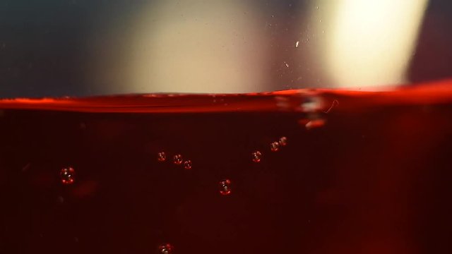 Somebody stirs red liquid with bubbles, using a metal spoon. x2 slow motion