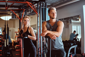 Fototapeta na wymiar Portrait of an attractive sportive couple posing while leaning on barbells, looking away in a fitness club or gym.