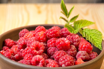 Fresh organic healthy raspberry with mint leaves in clay dish on wooden table background. Rustic style and natural light. food photo.