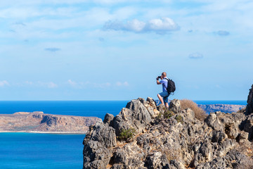 traveler with a backpack stands on a rock and takes pictures on