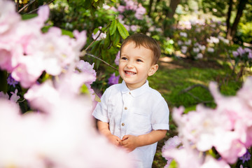 Cute little baby boy in pink flowers smile in summer outdoors
