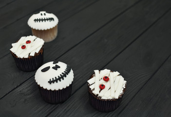 Halloween cupcakes. Mummy and jack-head cupcake. Halloween treats on black wood background.