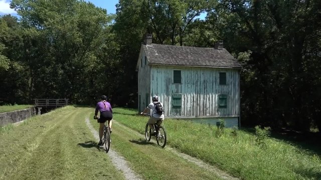 Mother and teen son bike past an old white wooden building on the C&O Canal National Historic Park near Harpers Ferry, West Virginia.