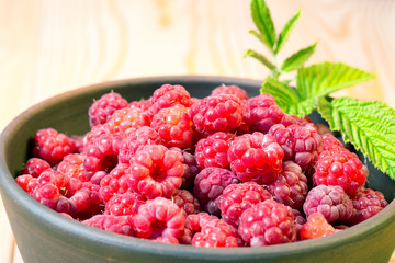 Fresh organic healthy raspberry with mint leaves in clay dish on wooden table background. Rustic style and natural light. food photo.