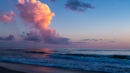 Sunrise over the ocean turns the sky, clouds and ocean so many different colors as waves break on the shore.