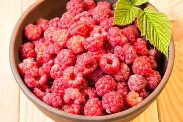 Fresh organic healthy raspberry with mint leaves in clay dish on wooden table background. Rustic style and natural light. food photo.