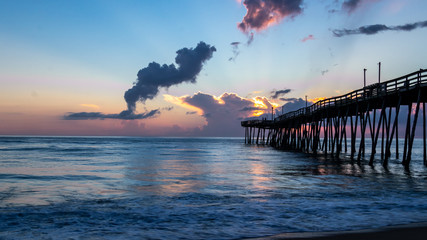 Fototapeta premium Dramatic morning sky as the sun rises over the Atlantic in the Outer Banks of North Carolina. The colorful sky reflected on the surface of the calm ocean water.